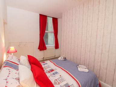A bedroom with a bed with red and white bedding red pillows a window with red curtains and folded towels on the bed at 1 Church Square in Whitby