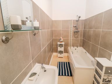 A bathroom with a bathtub, showerhead, sink, storage units, and a striped rug at 1 Church Square in Whitby