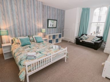 A bedroom with a bed and teal cushions and lamps a black sofa with cushions and large window at 1 Church Square in Whitby