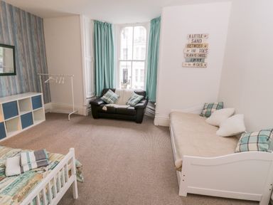 A room with two beds a black sofa a cubical shelf and a window with blue curtains at 1 Church Square in Whitby