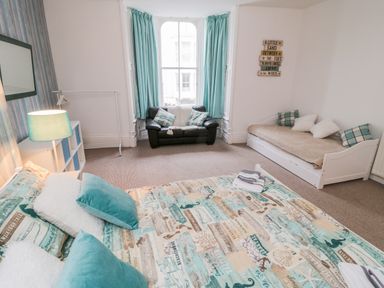 A bedroom with a double bed sofa bed black armchair and window with teal curtains at 1 Church Square in Whitby
