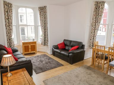 A living room with two black sofas and red pillows wooden furniture and patterned curtains at 1 Church Square in Whitby