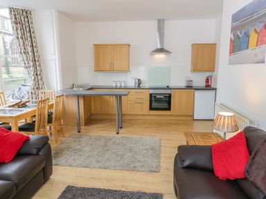 A kitchen with wooden cabinets and a dining table next to a living area with dark sofas and red pillows at 1 Church Square in Whitby