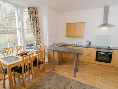 A kitchen with wooden cabinets a countertop with appliances and a dining table with chairs near large windows at 1 Church Square in Whitby