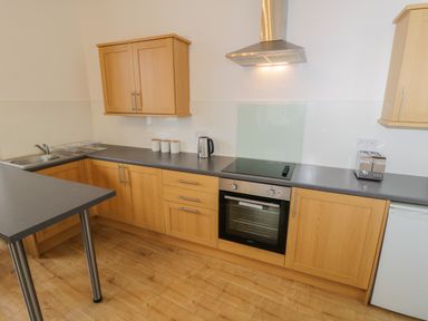A kitchen with wooden cabinets a black countertop a stainless steel oven a stovetop a toaster a kettle a sink and wooden flooring at 1 Church Square in Whitby