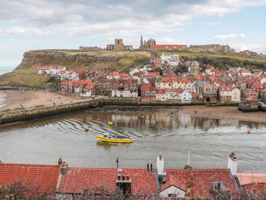 A coastal town with red roof houses a yellow boat in the water and a hill with historic buildings at 1 Church Square in Whitby