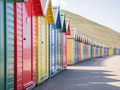 Rows of colorful wooden beach huts lined up along a paved pathway with a hill in the background at 1 Church Square in Whitby