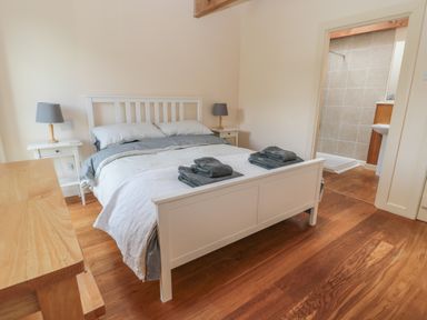 A bedroom with a white bed frame bedside tables with lamps wooden floor and an adjoining bathroom at The Long Barn in Berwick-Upon-Tweed