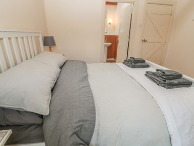 A bedroom with a double bed a bedside lamp folded towels and a door leading to a bathroom at The Long Barn in Berwick-Upon-Tweed