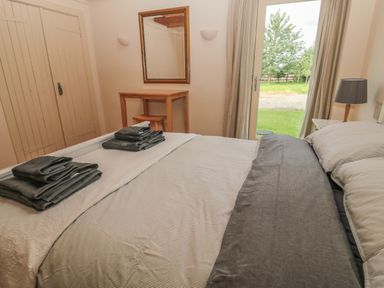 A bedroom with a made bed and towels on it a wooden dressing table with a stool a mirror and a door opening to a garden at The Long Barn in Berwick-Upon-Tweed