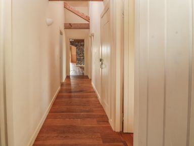 A hallway with wooden floor beams on the ceiling and doors along the walls at The Long Barn in Berwick-Upon-Tweed