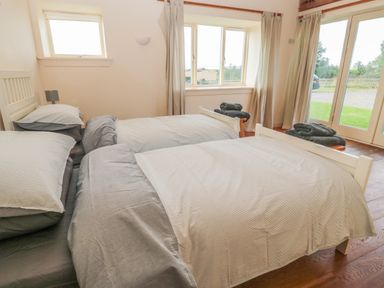A bedroom with two single beds and windows showing outdoor greenery at The Long Barn in Berwick-Upon-Tweed