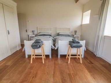 A bedroom with two single beds side by side each with a wooden stool holding folded towels at The Long Barn in Berwick-Upon-Tweed