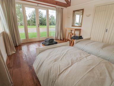 A bedroom with two single beds a wooden floor and glass doors leading outside at The Long Barn in Berwick-Upon-Tweed