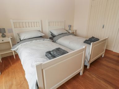 A bedroom with two single beds with grey bedding and folded towels with two bedside tables and lamps on wooden floor at The Long Barn in Berwick-Upon-Tweed