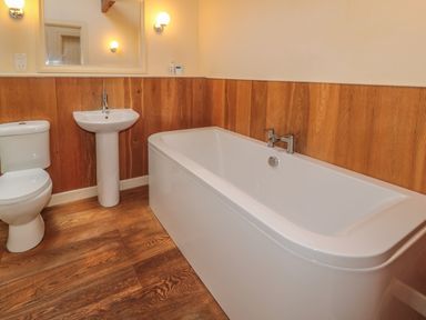 A bathroom with a toilet sink bathtub wooden paneling and lights at The Long Barn in Berwick-Upon-Tweed