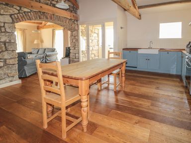 A kitchen with wooden table and chairs and blue cabinets connected to a living room with sofas at The Long Barn in Berwick-Upon-Tweed