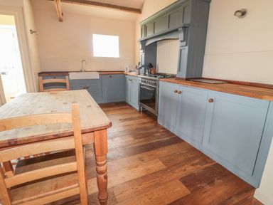 A kitchen with blue cabinets wooden countertops a wooden table and chairs and a window at The Long Barn in Berwick-Upon-Tweed