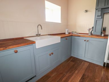 A kitchen with blue cabinets wooden countertops a white sink and a small window at The Long Barn in Berwick-Upon-Tweed