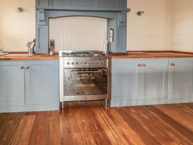 A kitchen with blue cabinets a stainless steel oven and wooden floors at The Long Barn in Berwick-Upon-Tweed