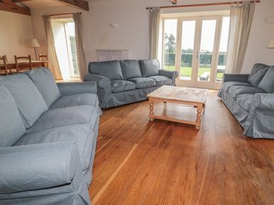 A living room with three blue sofas a wooden coffee table wooden floor and large glass doors at The Long Barn in Berwick-Upon-Tweed