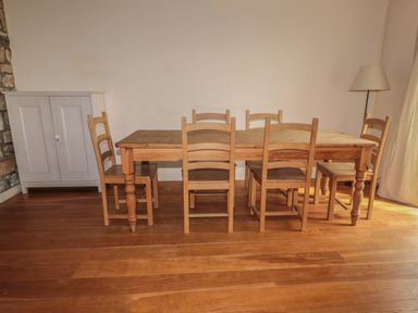 A wooden dining table with six chairs in a room with wooden floor and white walls at The Long Barn in Berwick-Upon-Tweed