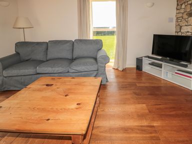 A living room with a grey sofa wooden coffee table TV on a white stand and a floor lamp at The Long Barn in Berwick-Upon-Tweed