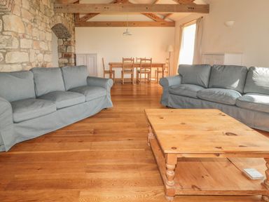 A living room with two sofas and a wooden coffee table and a dining table with chairs in the background at The Long Barn in Berwick-Upon-Tweed