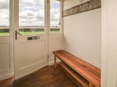 An entryway with a wooden bench and wall hooks next to glass doors overlooking a field at The Long Barn in Berwick-Upon-Tweed