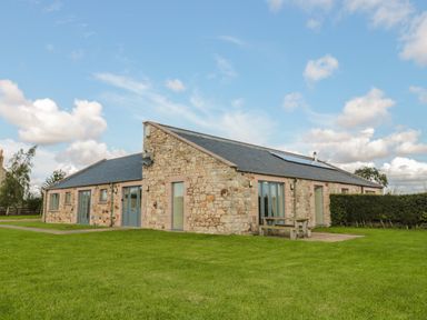 A stone building with multiple glass doors and a picnic table on grass at The Long Barn in Berwick-Upon-Tweed