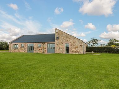 A single-story stone house with multiple windows and doors on a green lawn at The Long Barn in Berwick-Upon-Tweed