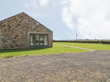 Stone building with glass doors on a lawn with gravel in front at The Long Barn in Berwick-Upon-Tweed