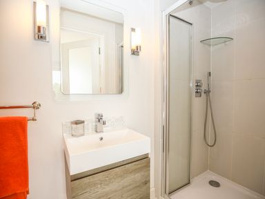 A bathroom with a rectangular sink vanity a mirror two wall lights and a shower enclosure at Shutts House Garden Apartment in Coombe Bissett