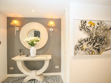 A hallway with a stone console table with a round mirror above two wall lamps and abstract painting on the side wall at Shutts House Garden Apartment in Coombe Bissett