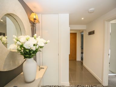 A hallway with a vase of white flowers on a table and a round wall mirror at Shutts House Garden Apartment in Coombe Bissett