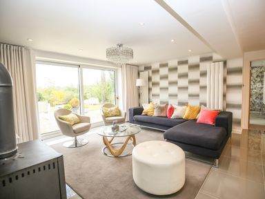 A living room with a black sectional sofa with colorful cushions two grey chairs a round glass coffee table and a white ottoman at Shutts House Garden Apartment in Coombe Bissett
