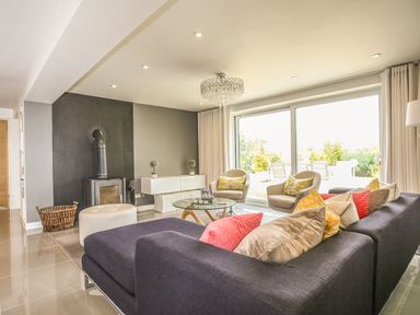 A living room with a dark sofa and colorful cushions two beige chairs a glass coffee table and a wood stove at Shutts House Garden Apartment in Coombe Bissett