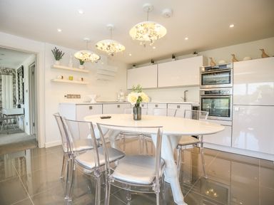 A kitchen with a white oval table and clear chairs surrounded by white cabinets and stainless steel ovens at Shutts House Garden Apartment in Coombe Bissett