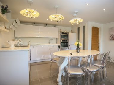 A kitchen with a round table and transparent chairs under three ceiling lights at Shutts House Garden Apartment in Coombe Bissett