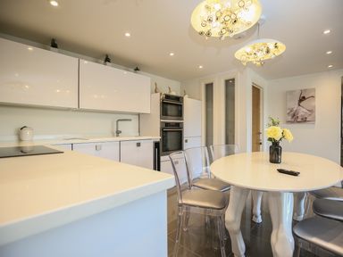A kitchen with a round table with flowers in a vase and transparent chairs at Shutts House Garden Apartment in Coombe Bissett