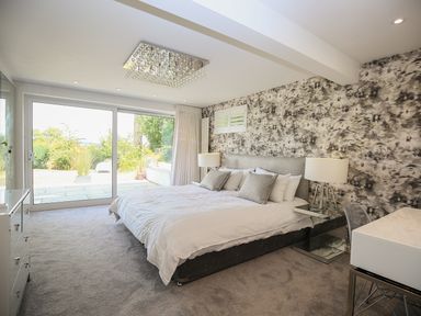 A bedroom with a large bed nightstands lamps a desk chair and sliding glass doors opening to a garden at Shutts House Garden Apartment in Coombe Bissett