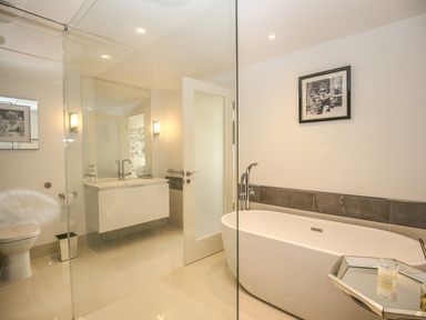 A bathroom with a freestanding bathtub a floating vanity a toilet and framed pictures at Shutts House Garden Apartment in Coombe Bissett