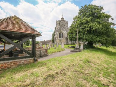 A church with gravestones and a large tree near a covered wooden structure at Shutts House Garden Apartment in Coombe Bissett