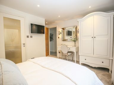 A bedroom with a bed a white wardrobe a dressing table with a mirror and chair and a wall-mounted television at Shutts House Garden Apartment in Coombe Bissett
