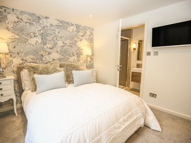 A bedroom with a bed with pillows and lamps on nightstands and a door leading to a bathroom at Shutts House Garden Apartment in Coombe Bissett