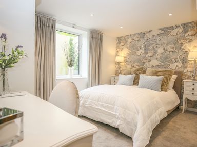 A bedroom with a double bed with white bedding and decorative pillows beside two bedside tables with lamps and a window with curtains at Shutts House Garden Apartment in Coombe Bissett