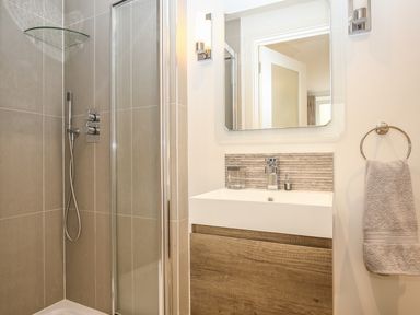 A bathroom with a shower area glass shower door wooden vanity basin mirror and a towel hanging on a ring at Shutts House Garden Apartment in Coombe Bissett