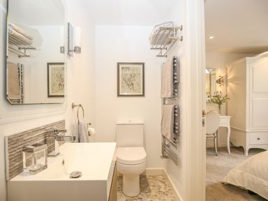 A bathroom with a toilet sink mirror towels and a framed picture next to a bedroom with a desk chair and wardrobe at Shutts House Garden Apartment in Coombe Bissett