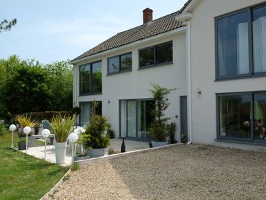 The exterior of a two-story house with large windows a gravel area and a patio with potted plants at Shutts House Garden Apartment in Coombe Bissett