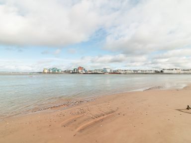 A sandy beach with calm water and buildings across the water at Sea Point in Exmouth